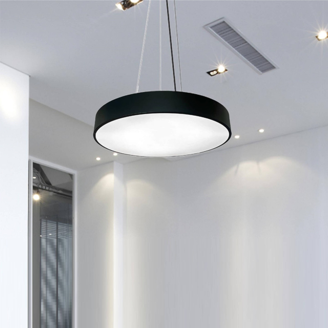 A contemporary circular pendant light suspended from the ceiling by thin metal cables, providing bright, uniform illumination for an office or commercial space.